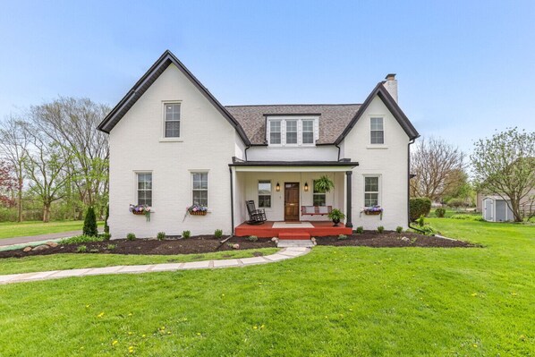 A two-story house with a front porch, a small garden, and a pathway leading to the entrance.