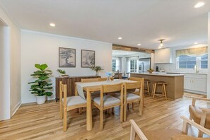 A modern kitchen with wooden cabinets, a central island, and a dining area with a wooden table and chairs.