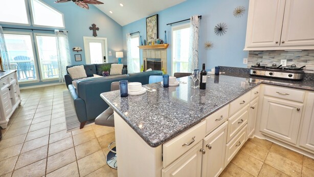 A kitchen with granite countertops, white cabinets, a ceiling fan, and a large window. - Blue Pearl Walk to Beach Sleeps 9 New Golf Cart Option (Bolivar Peninsula)