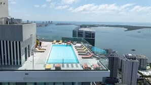 Une piscine sur le toit, dotée de chaises longues et offrant une vue sur la ville et l’eau.