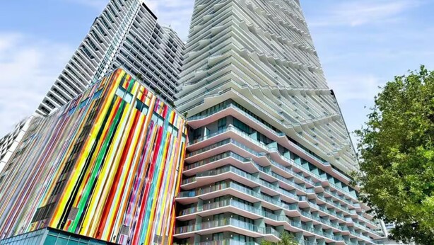 Un immeuble moderne de grande hauteur, doté d’une façade remarquable caractérisée par un motif de bandes verticales aux couleurs vives.