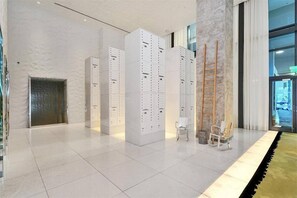 Eine moderne Lobby mit weißen Schließfächern, einer Holzleiter und einer Glastür zum Außenbereich.