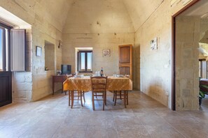 Un comedor con una mesa dispuesta para cuatro, televisión y paredes de piedra.
