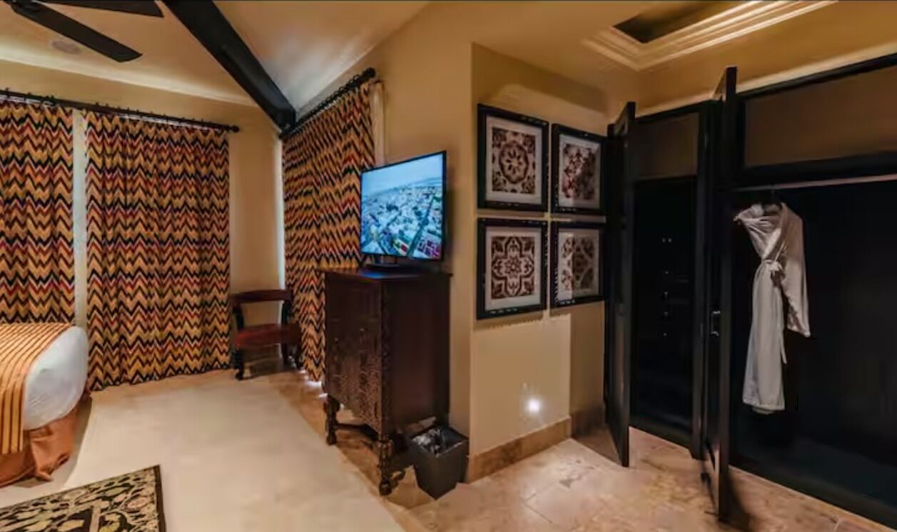 Una habitación con televisión, cortinas estampadas, cama, armario y cuadros en la pared.