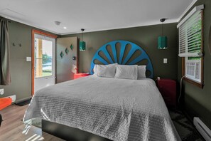A bedroom with a large bed, a modern headboard, a nightstand, a red cabinet, a window with blinds, and a view of greenery outside. - Berkshire Lake Lodge  (Lee)