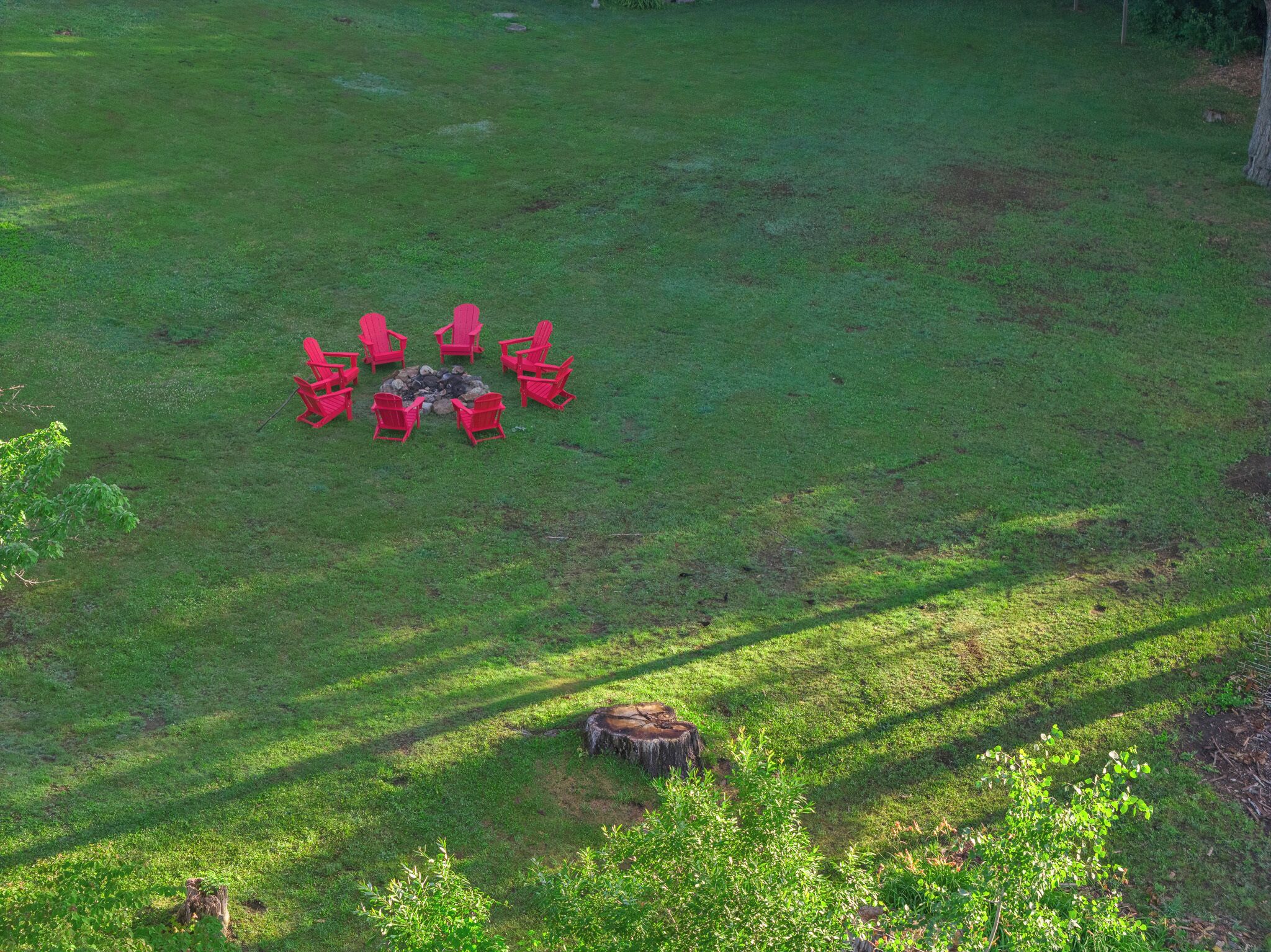 A grassy outdoor area with a fire pit and red chairs arranged in a circle.