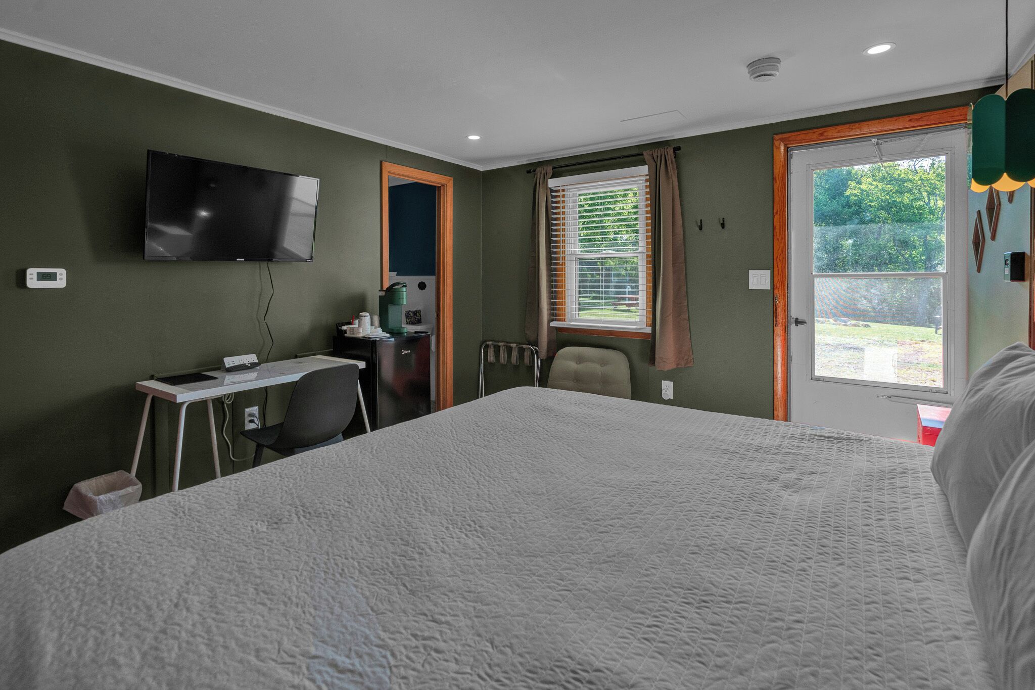 Ein Hotelzimmer mit einem Bett, einem Schreibtisch, einem Stuhl, einem Fernseher und einem Fenster mit Jalousien.
