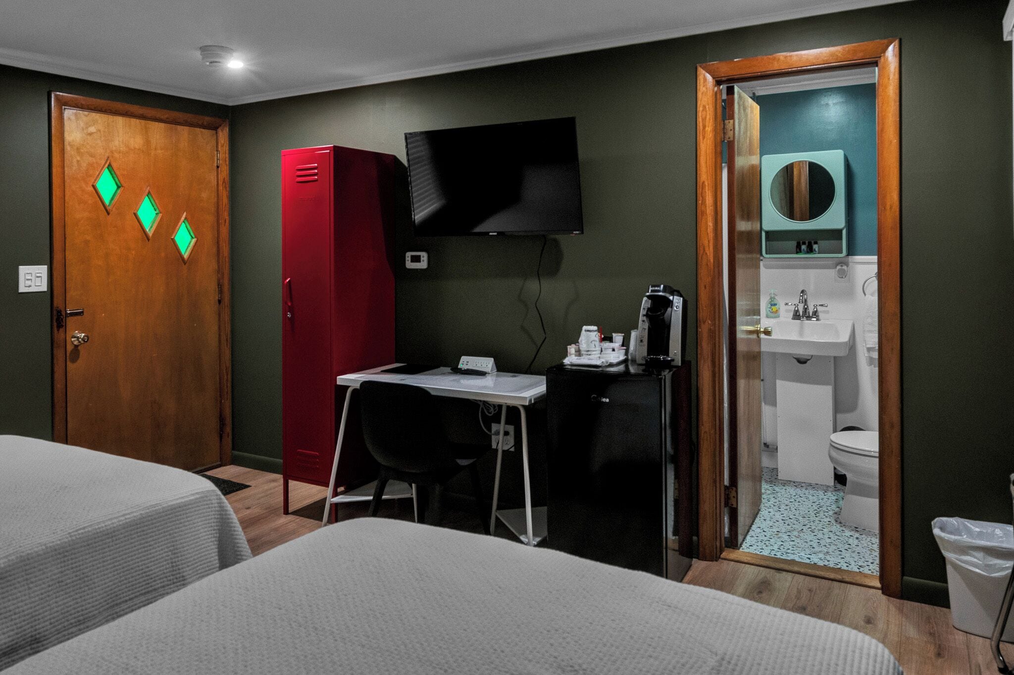 A hotel room with two beds, a desk with a chair, a television, a red wardrobe, and a bathroom with a sink and toilet.