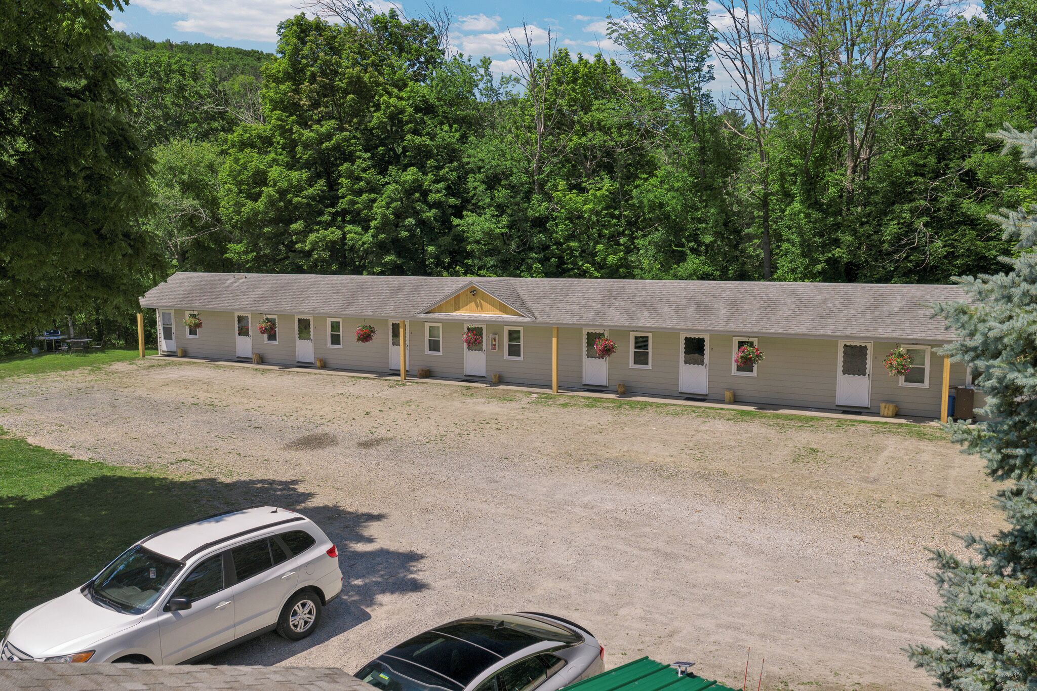A motel with multiple rooms, a gravel parking area, and a car parked in front.