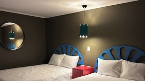 Una habitación con dos camas, un espejo redondo, una caja roja y una lámpara colgante.