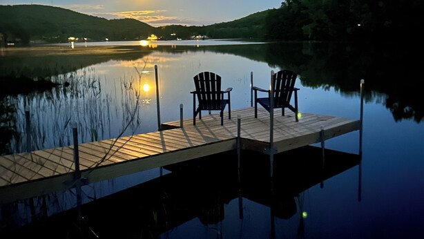 Un lago tranquilo al anochecer, con un muelle de madera y dos sillas mirando al agua.