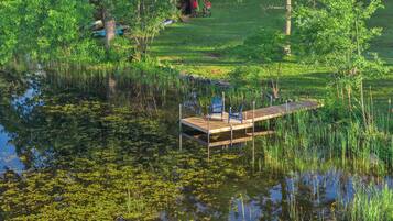 A wooden dock extending into a pond surrounded by lush greenery and trees.