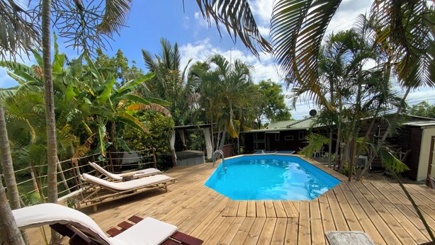 A wooden deck with a swimming pool, lounge chairs, and tropical vegetation. - La Casa 974 (Saint-Pierre)