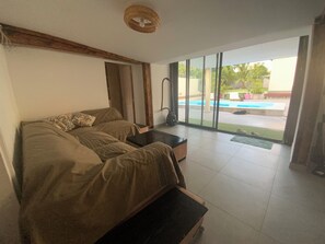 A room with a sofa, a small table, and a view of an outdoor swimming pool.