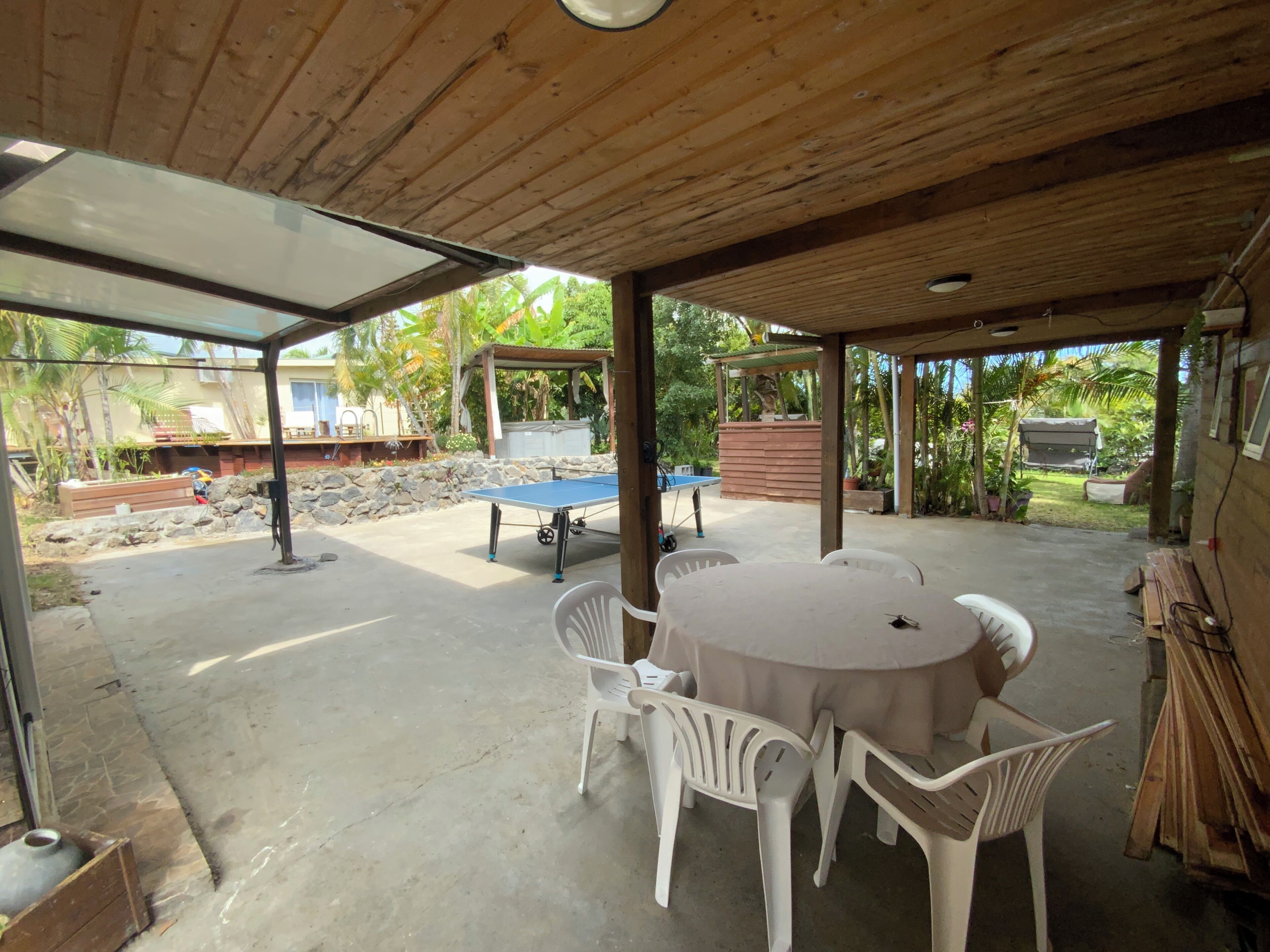 A covered patio area with a ping pong table, white plastic chairs, and a concrete floor.