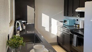 A modern kitchen with a black countertop, stainless steel appliances, and a window providing natural light. - 2Bed1Bath Mostaccioli KingQueenBeds CentralPhoenix (Phoenix)