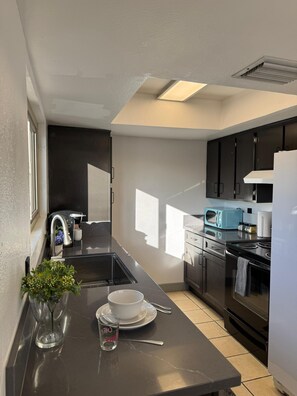 A modern kitchen with a black countertop, stainless steel appliances, and a window providing natural light. - 2Bed1Bath Mostaccioli KingQueenBeds CentralPhoenix (Phoenix)