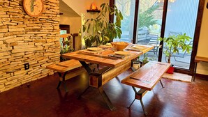 A dining area with a stone wall, a wooden table set for four, and a large window with a view. - The Stone & Bridge: Close to MKT Trail & Dog Park, Dining, Groceries & I-70 (Columbia)