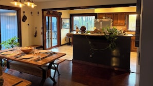 A modern kitchen with a central island, wooden cabinetry, and a dining area with a large table and benches. - The Stone & Bridge: Close to MKT Trail & Dog Park, Dining, Groceries & I-70 (Columbia)