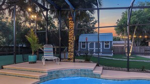 Une piscine avec un patio couvert, une petite maison et une cour clôturée.