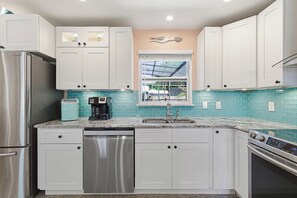 A kitchen with white cabinets, a stainless steel refrigerator, a dishwasher, a coffee maker, and a window with a view of the outdoors. - 🌞🌴Pet Friendly Home w/ Private Pool + Fenced Yard | Sunny Dayz🌴🌞 (New Smyrna Beach)