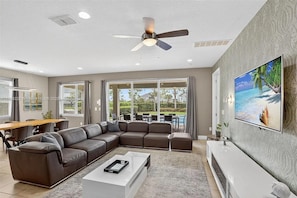 A modern living room with a sectional sofa, a coffee table, a ceiling fan, and a large TV on the wall. - Stupendous Disney Vacation Home W Private Pool (Kissimmee)