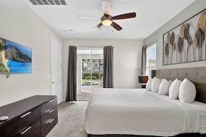 A bedroom with a bed, a ceiling fan, a TV, a painting, and a view of the outdoors. - Stupendous Disney Vacation Home W Private Pool (Kissimmee)