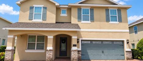 A two-story house with a garage, a front entrance with a door, and a brick driveway.