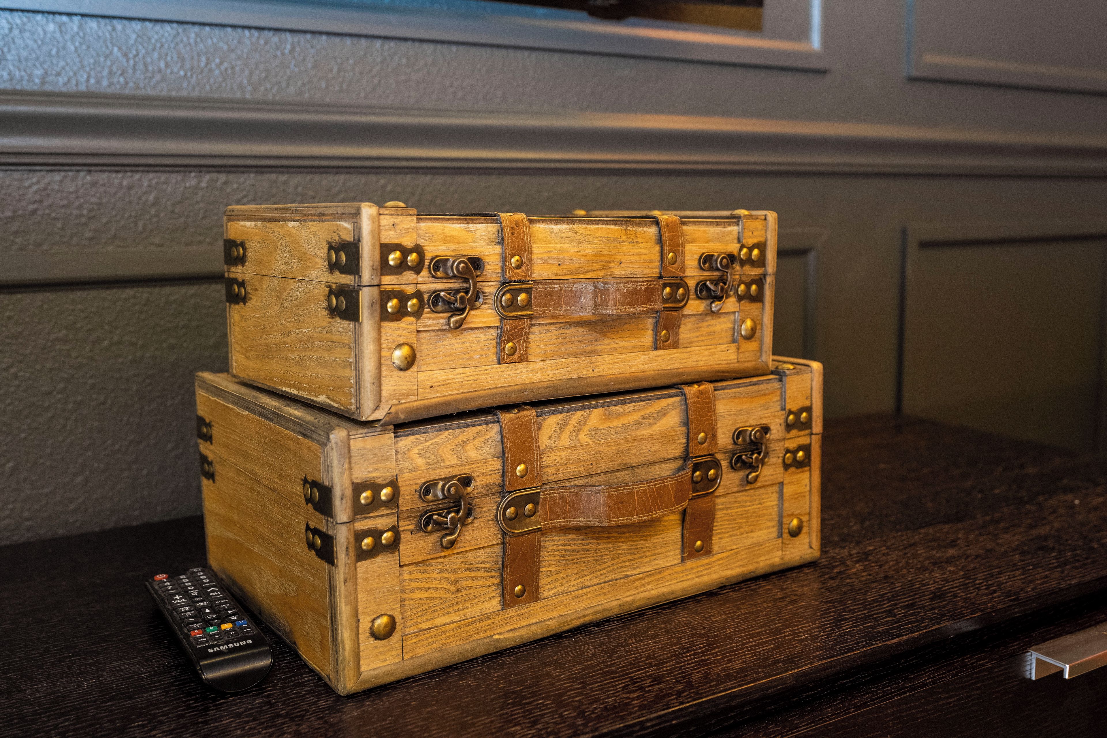 A stack of wooden trunks with metal clasps and a remote control on a dark wooden surface.