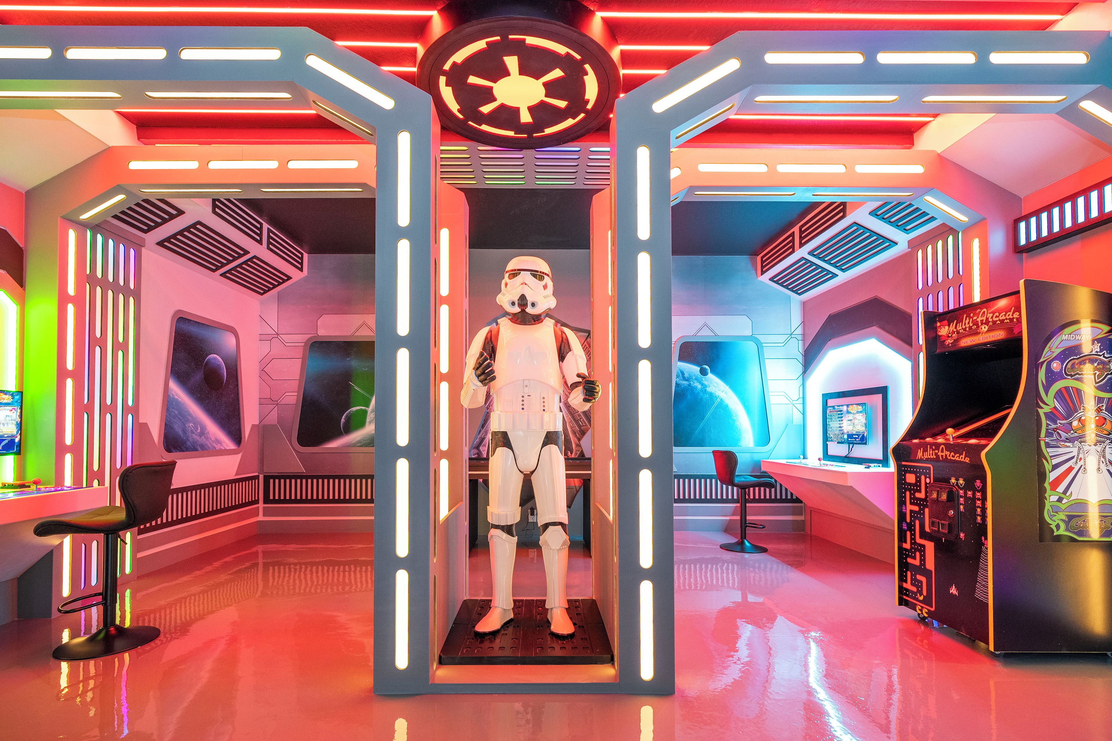 Une pièce futuriste avec une figure centrale, un éclairage néon et des bornes d’arcade.