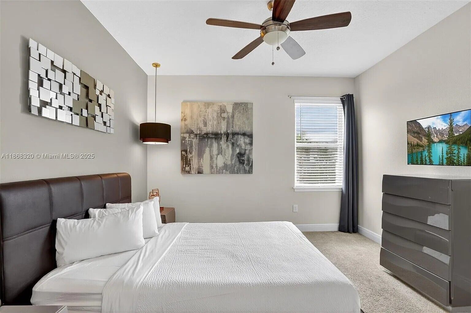 A bedroom with a bed, a ceiling fan, a painting, a TV, and a dresser.