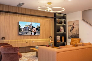 A modern living room with a flat-screen TV mounted on a wooden wall, a sofa, a coffee table, and decorative items. - Stupendous Disney Vacation Home W Private Pool (Kissimmee)