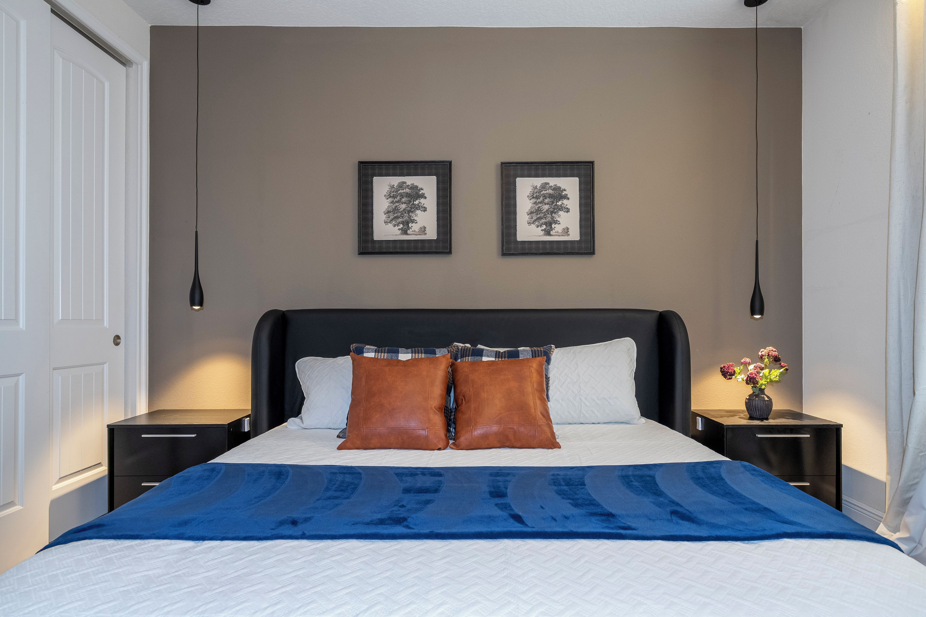 A bedroom with a bed, two nightstands, a dresser, a window with curtains, and two framed pictures on the wall.