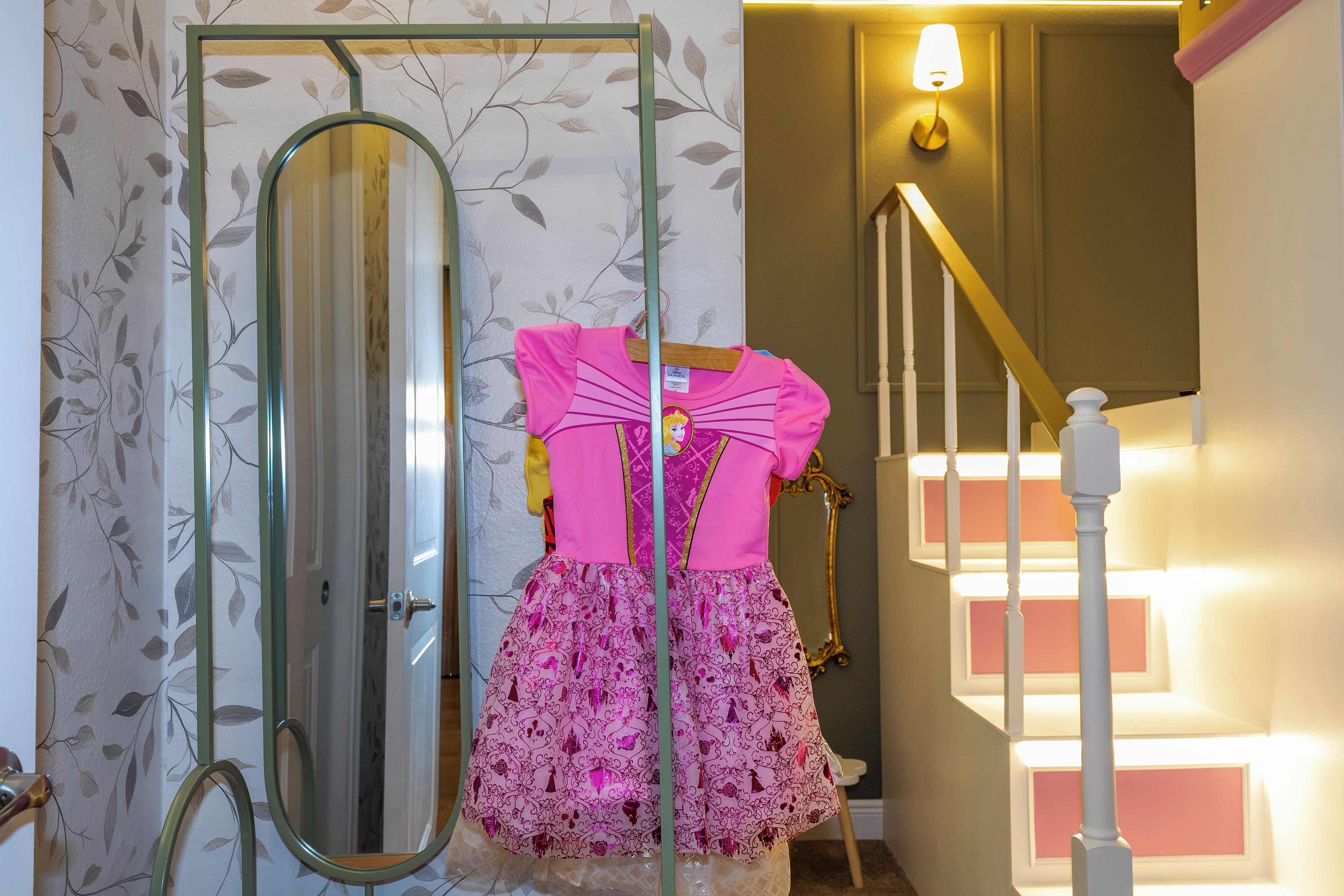 A room with a mirror, a staircase, and a pink dress on a hanger.
