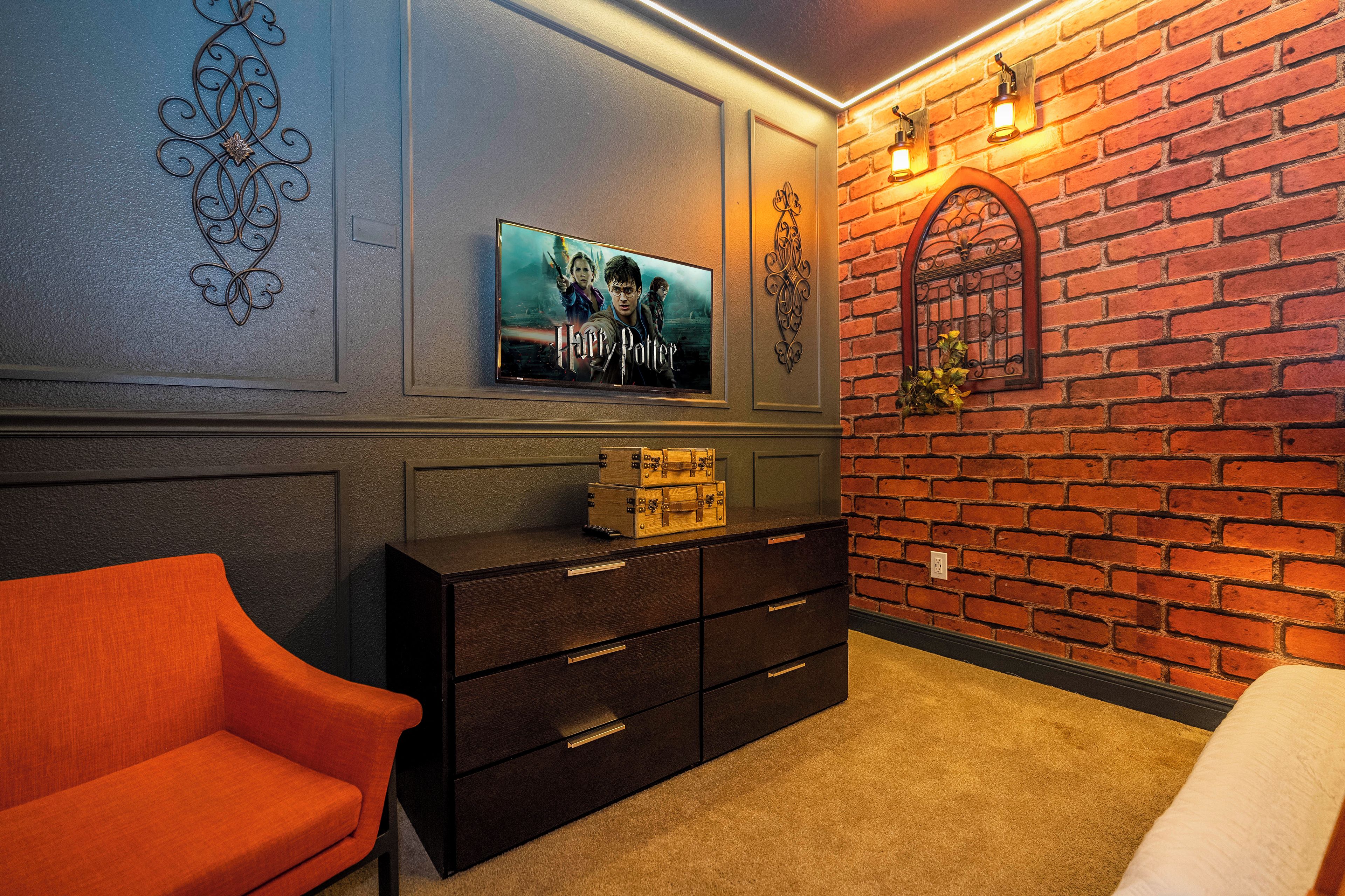 A room with a brick wall, a television mounted on the wall, a wooden dresser, and a red chair.