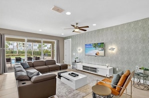 A modern living room with a sofa, coffee table, TV, and a balcony with a view. - Stupendous Disney Vacation Home W Private Pool (Kissimmee)
