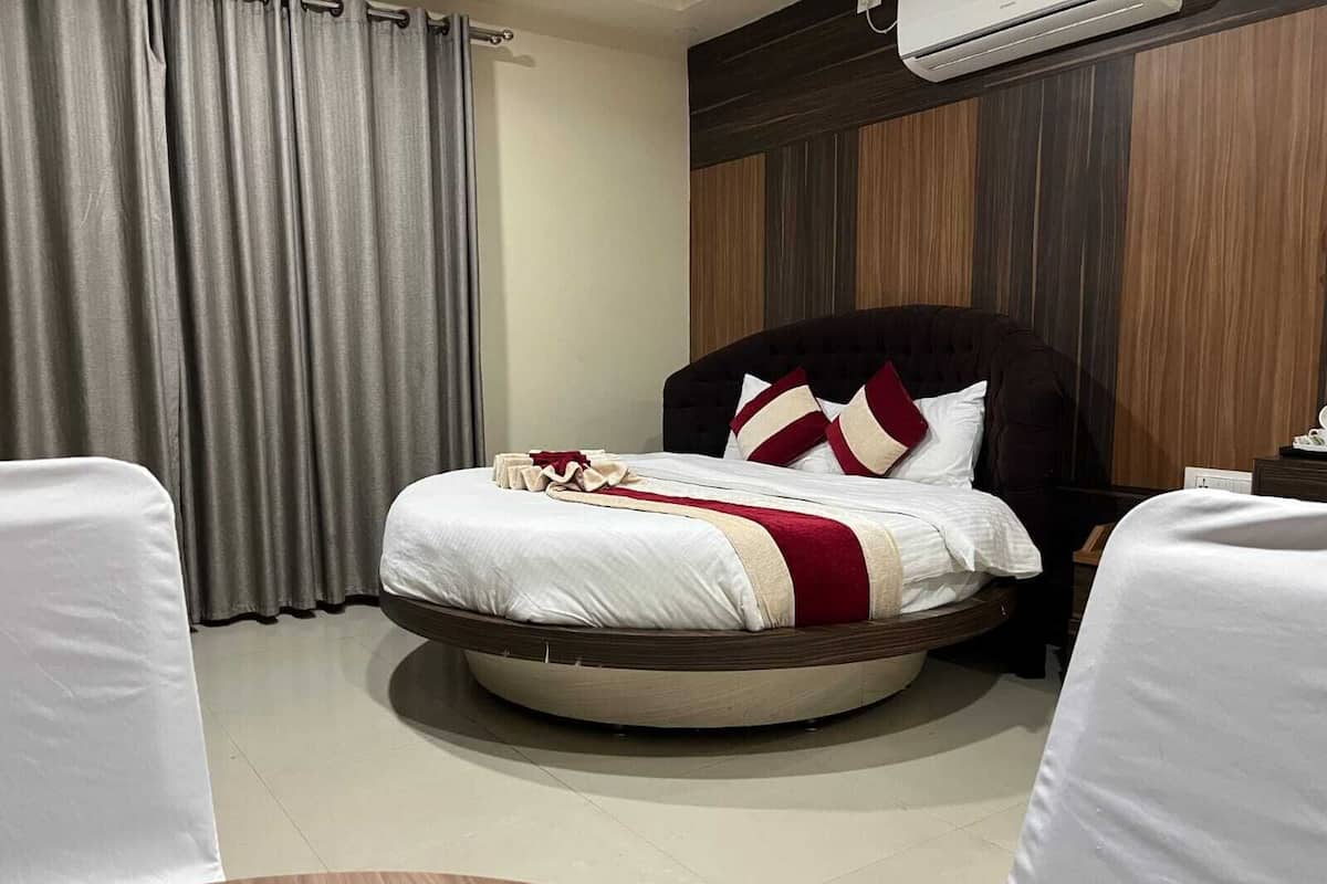 A hotel room with a round bed, a bedside table, a chair, a curtain, and an air conditioning unit.