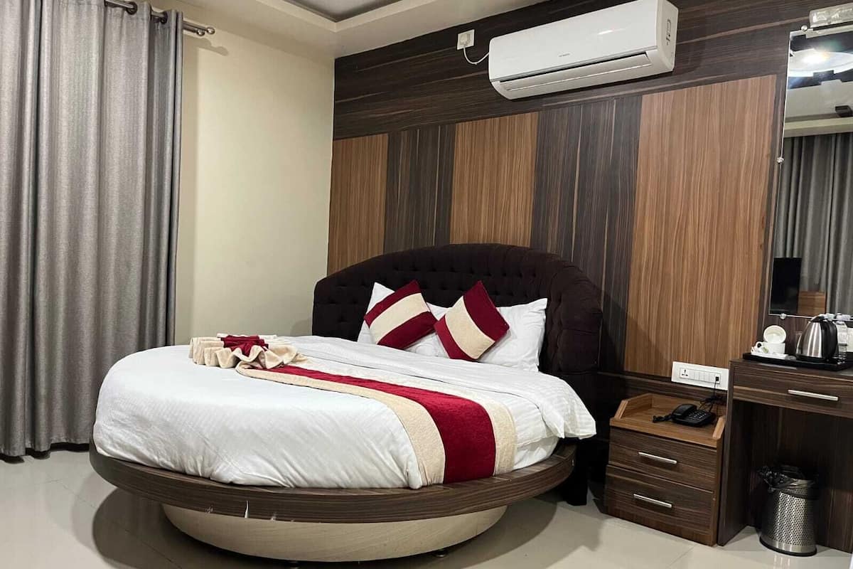 A circular bed with a dark headboard, a white and red bedspread, and a wooden nightstand with a phone and a trash can.