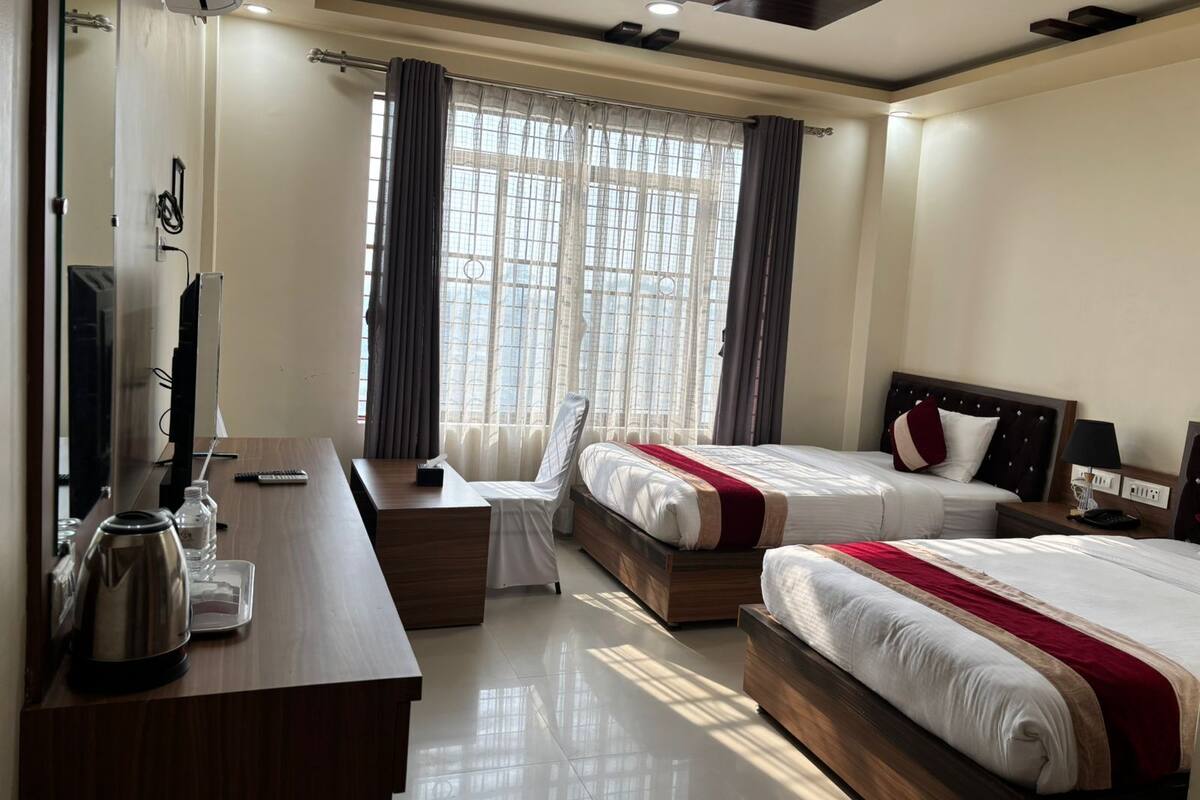 A hotel room with a desk, two beds, a TV, and a window with curtains.