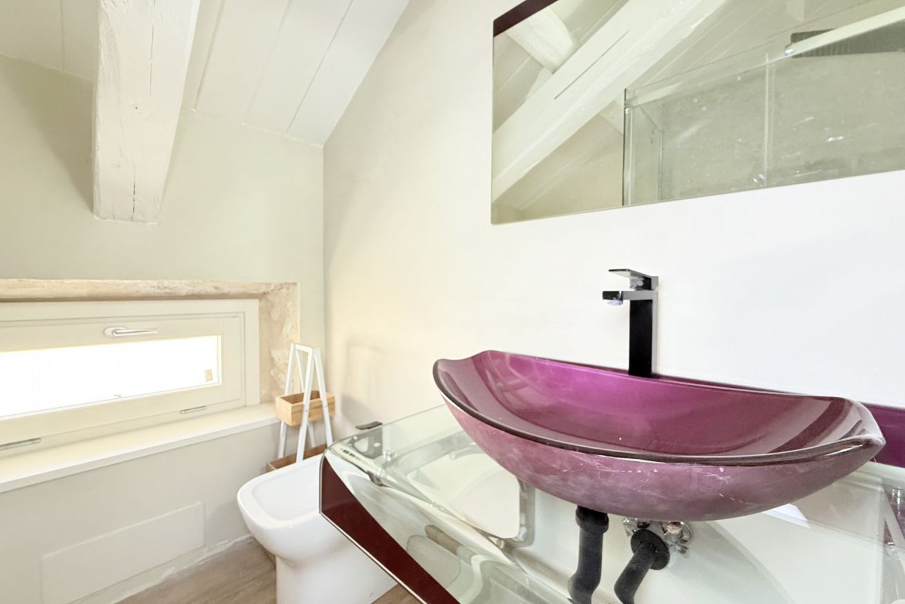 A bathroom with a glass basin, a white toilet, a window, and a mirror.