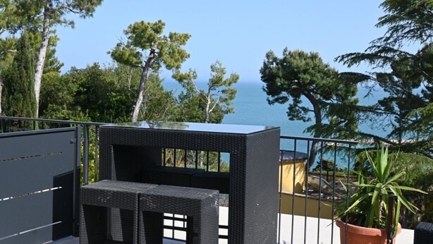 Ein Balkon mit einem Korbstuhl-Set, einem Blumentopf und Blick auf das Meer.