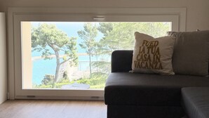Ein Zimmer mit Blick auf ein Gewässer, ein Sofa mit Kissen und ein Fenster mit Blick auf Bäume und ein Gebäude.