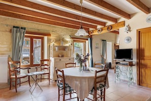 Un coin repas avec une table ronde, des chaises, un téléviseur et, au fond, une cuisine.