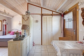 A bedroom with a bed, a dresser, a wooden ceiling, and a window with curtains.