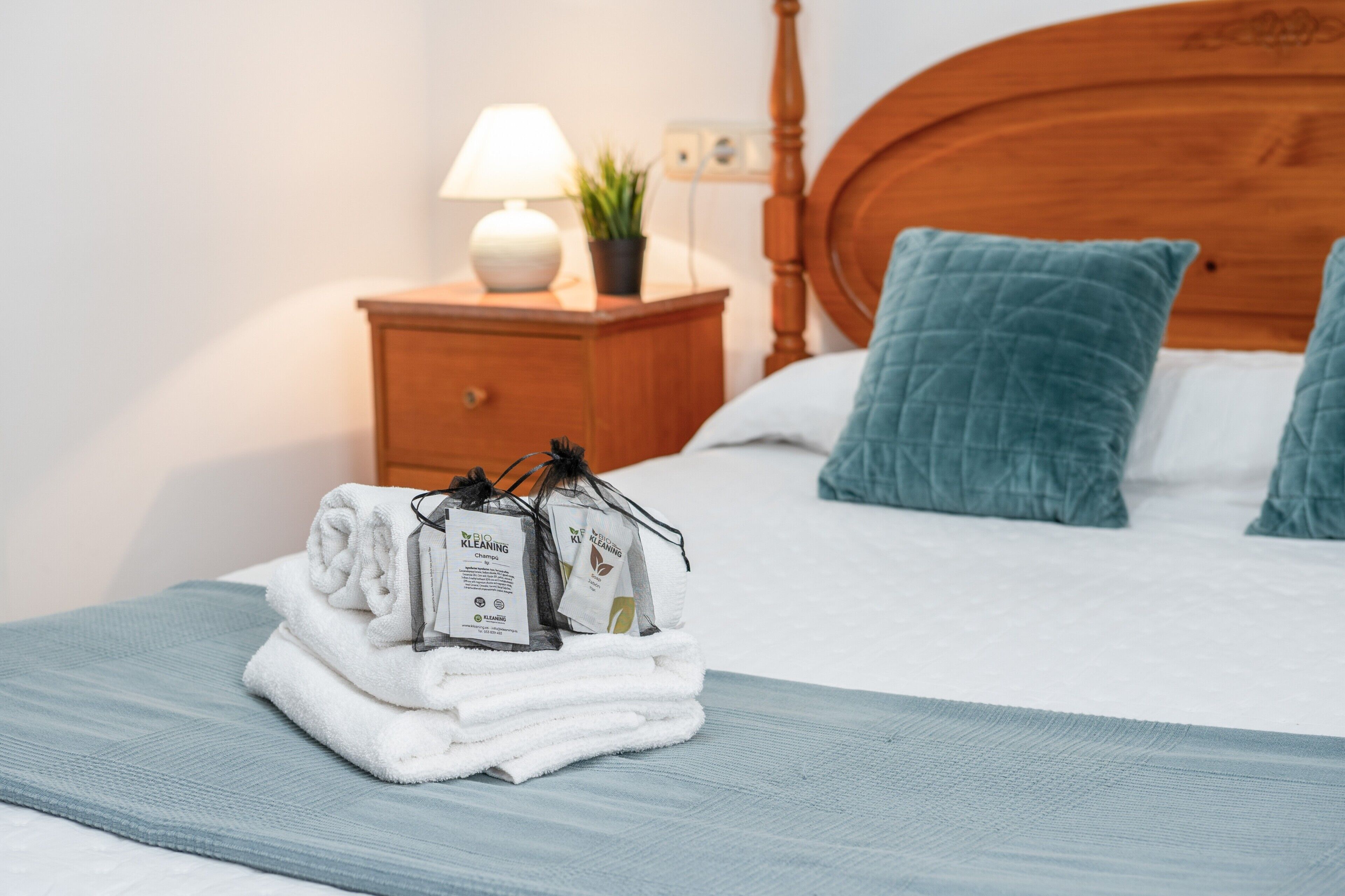 Een net opgemaakt bed met een blauw sprei, een houten hoofdbord en twee blauwgroene kussens.