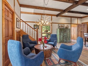 A spacious room with a wooden staircase, blue armchairs, a round wooden coffee table, and a rustic chandelier. - Thulite Chalet - 20-NCD0315 (Estes Park)