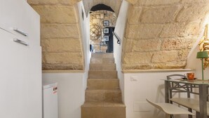 Eine enge Treppe führt zu einem Raum mit einer Steinwand, einem kleinen Tisch mit Stühlen und einem Kühlschrank.