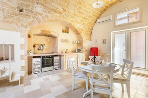A kitchen with a brick arch, white cabinetry, a red appliance, and a dining area with white chairs. - Casa del Grano by BarbarHouse (Alessano)