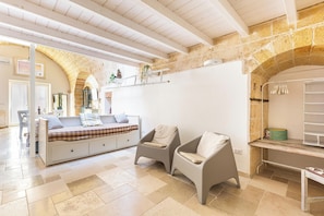 A room with a bed, two armchairs, a white sofa, a stone wall, and a tiled floor. - Casa del Grano by BarbarHouse (Alessano)