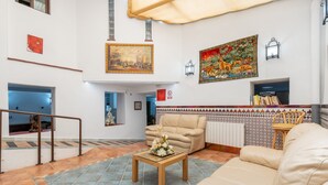 Un vestíbulo amplio con un sofá, una mesa de centro con flores, un cuadro, piso de baldosas y pared con diseño.